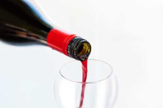 Pouring red wine from bottle into the wineglass on white background. Blurred concept