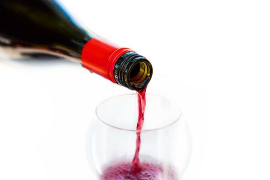 Pouring red wine from bottle into the wineglass on white background. Blurred concept
