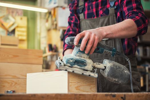 Worker grinds the wood box of angular grinding machine