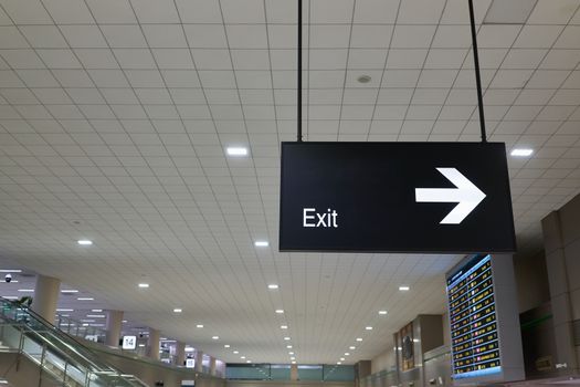Exit and arrow information board sign with white character on black background at international airport terminal.
