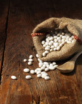 White beans in bag with wooden spoon on wooden background