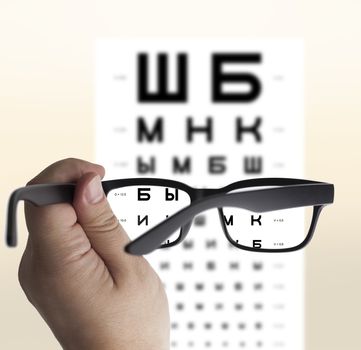 Eyeglasses in hand for eyesight Russian/Cyrillic test chart background, isolated