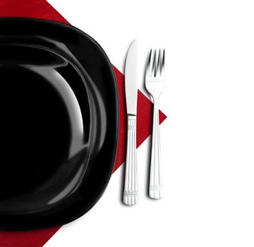 Black plate, fork and knife on red napkin. Isolated on white.