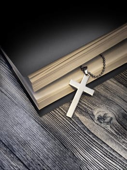 Metal cross on top of a black book cover on wooden background