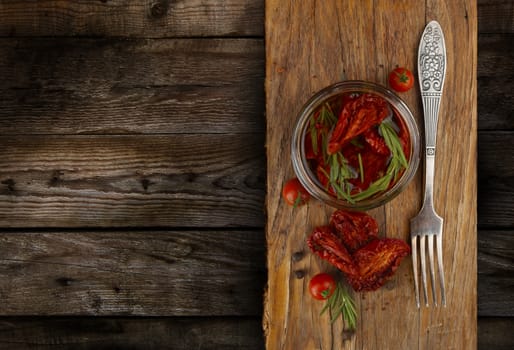Delicious dried tomatoes in the jar of olive oil, the fork on wood background. In rustic style. With a space for text.