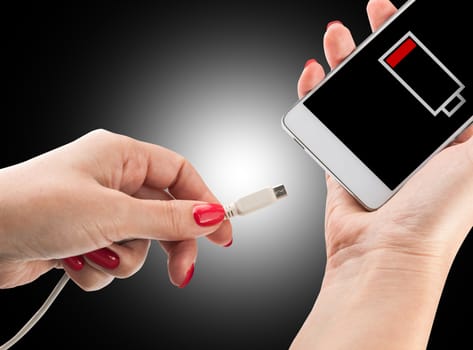 Female hand holding low battery smartphone and connect charger isolated on black background