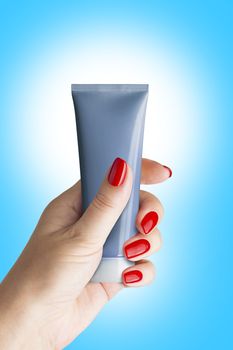 Plastic tube for cosmetics and body care in a female hand, isolated. Isolated on blue background. With clipping path