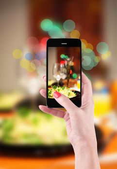 Female hand holding smartphone to take pictures of food and table setting