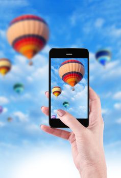 Female Hands Holding Smart Phone Displaying Photo of Blue Sky with Hot Air Balloons Behind.