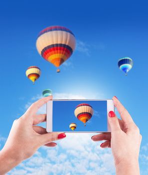 Female Hands Holding Smart Phone Displaying Photo of Blue Sky with Hot Air Balloons Behind.