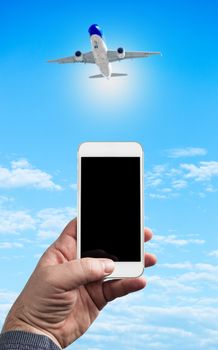 Man Hand holding using mobile phone and airplane on a blue background