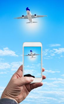 Man Hand holding using mobile phone and airplane on a blue background