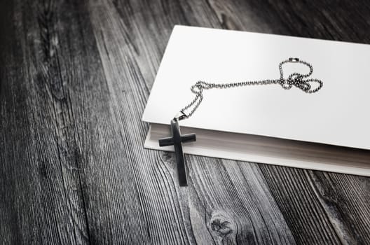 Metal cross on top of a white book cover on wooden background