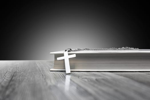 Metal, religious Christian cross with a book on a wooden background close up.