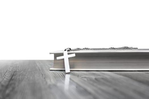 Metal cross on top of a white book cover on wooden background