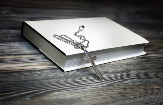 Metal cross on top of a white book cover on wooden background