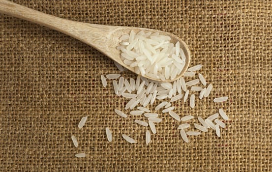 Asian uncooked white rice in a wooden spoon on a background of rough cloth