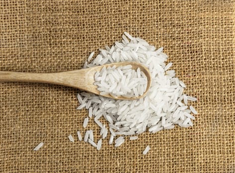 Asian uncooked white rice in a wooden spoon on a background of rough cloth