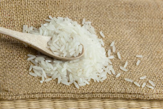 Asian uncooked white rice in a wooden spoon on a background of rough cloth