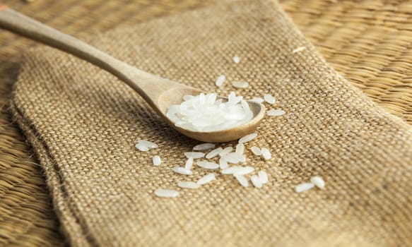Asian uncooked white rice in a wooden spoon on a background of rough cloth