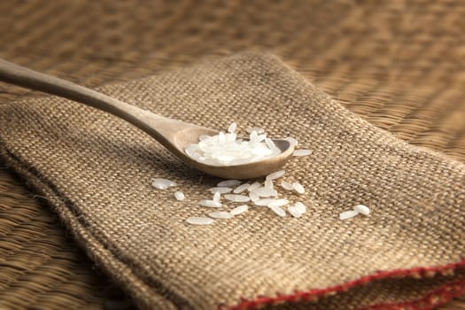 Asian uncooked white rice in a wooden spoon on a background of rough cloth