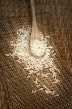 Asian uncooked white rice in a wooden spoon on a background of rough cloth