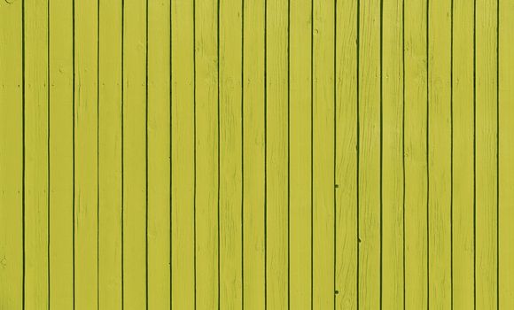 Wooden slat fence with parallel planks with yellow paint.