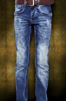 Blue jeans for the teenager with a belt. On a dark yellow background wood texture. With clipping path