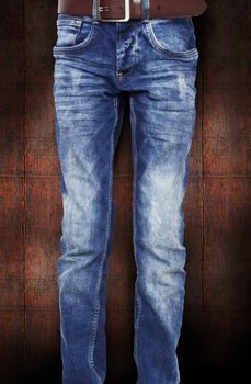 Blue jeans for the teenager with a belt. On a dark red background wood texture. With clipping path