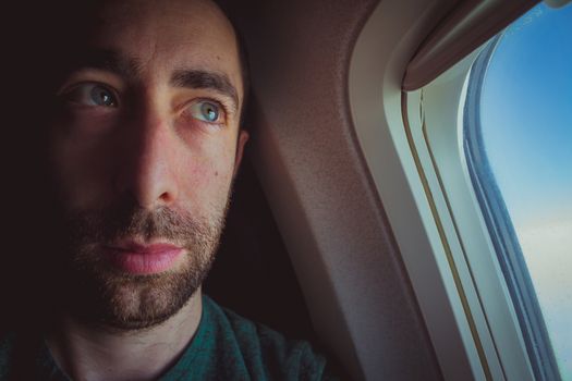 Close up of a pensive man looking outside through the window of an airplane.