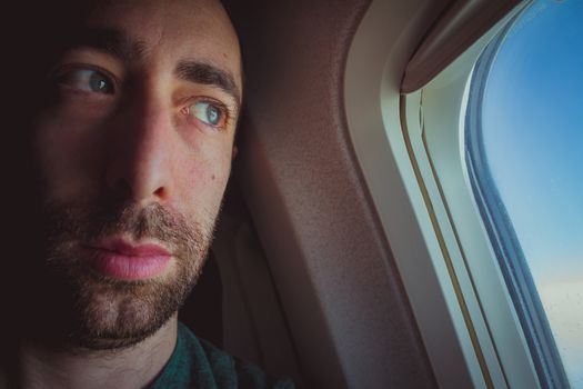 Close up of a pensive man looking outside through the window of an airplane.