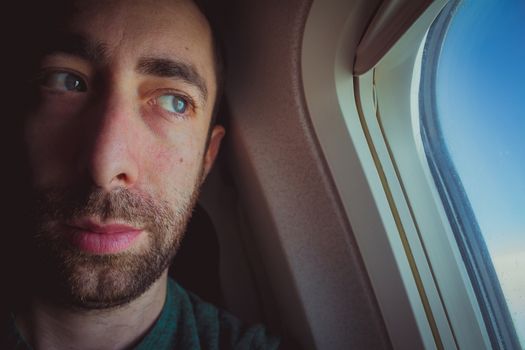 Close up of a pensive man looking outside through the window of an airplane.