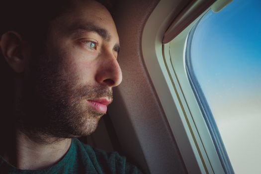 Close up of a pensive man looking outside through the window of an airplane.