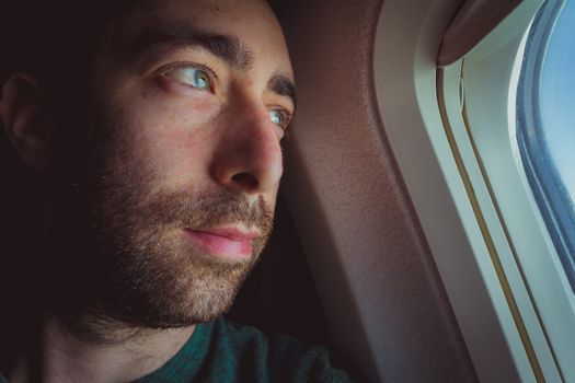 Close up of a pensive man looking outside through the window of an airplane.