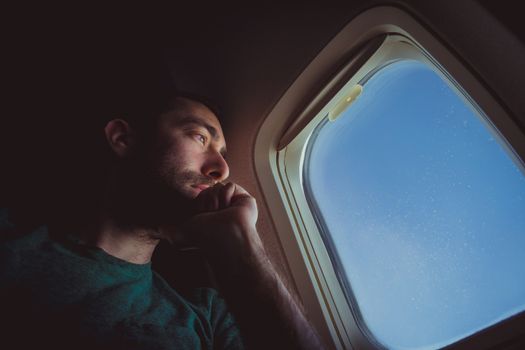 Pensive man looking outside through the window of an airplane.