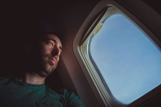 Pensive man looking outside through the window of an airplane.