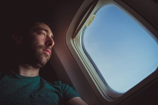 Pensive man looking outside through the window of an airplane.