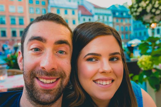 Happy young couple taking a selfie with a smartphone or camera in the street. They smiling and looking at the camera.