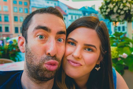 Happy young couple taking a selfie with a smartphone or camera in the street. They making silly and funny faces.