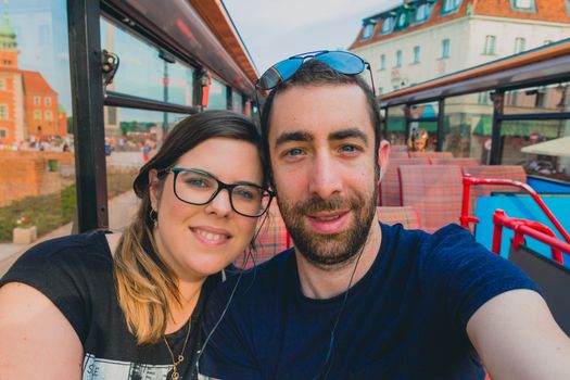 Happy couple taking a selfie with smartphone or camera inside a city tour bus.