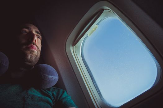 Pensive man with neck pillow seat by the window of an airplane.