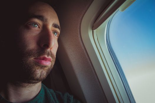 Close up of a pensive man seat by the window of an airplane.