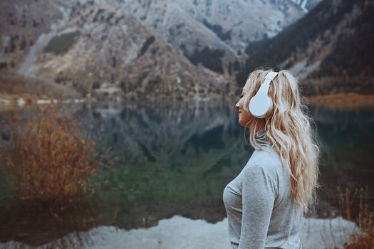 Woman wearing wireless headphones at the mountain lake