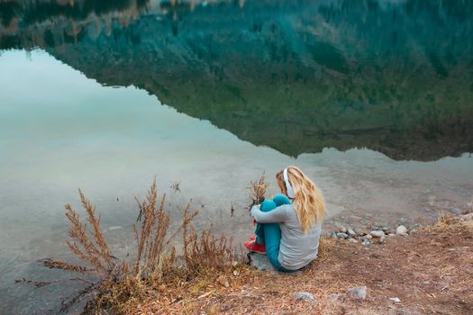 Woman listening music at the water's edge of mountain lake