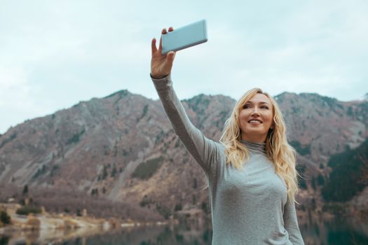 Smiling woman makes selfie at the mountain lake