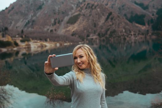 Smiling woman makes selfie at the mountain lake