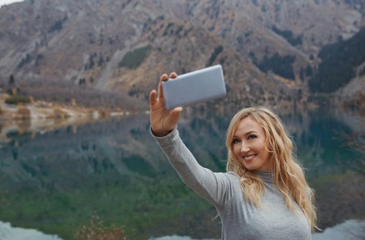 Smiling woman makes selfie at the mountain lake