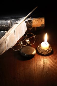 Vintage still life with quill pen and spectacles on old books near lighting candle