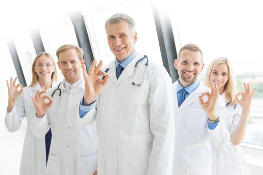 Successful team of medical doctors are looking at camera and showing ok sign