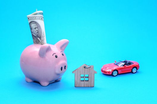 Pink piggy piggy bank with a house and a car on the table. Tinted. Concept of saving finances and real estate deposits